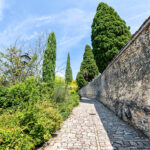 Via San Damiano street, road, stone walkway, path pedestrian trail at monastery in Assisi, Italy with wall, old, ancient, antique architecture, Italian landscape, cypress trees in summer